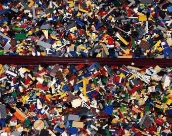 May include: A large collection of colorful Lego bricks in a plastic container. The bricks are a mix of different sizes, shapes, and colors, including red, blue, green, yellow, and black.