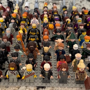 May include: A collection of Lego minifigures, featuring a variety of characters. The figures are arranged on a grey baseplate, showcasing a diverse array of colours and designs. The collection includes figures with wands, hats, and other accessories.