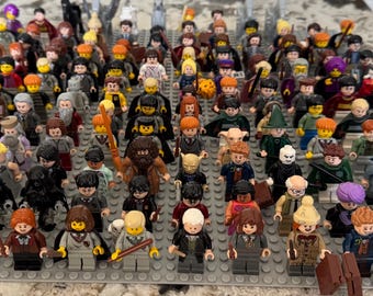Puede incluir: Una colección de minifiguras de Lego, con una variedad de personajes. Las figuras están dispuestas sobre una placa base gris, mostrando una diversa gama de colores y diseños. La colección incluye figuras con varitas, sombreros y otros accesorios.