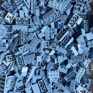 May include: A large collection of light gray plastic building bricks in various shapes and sizes. The pile includes rectangular blocks with multiple studs, flat plates, and specialized pieces, all featuring a uniform matte finish and hollow undersides.