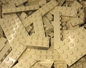 Peut inclure: Un tas de briques de construction beige clair, de différentes formes et tailles. Les briques ont un design classique avec des tenons circulaires sur le dessus pour se connecter. L'image montre une variété de briques rectangulaires et carrées.