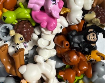 May include: A collection of colorful plastic animal figurines, including a pink pig, yellow tiger, brown bear, and green frog. The toys are in various poses and sizes, suitable for children's play or collecting.