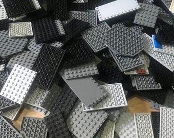 May include: A large collection of plastic building block plates in various rectangular and square shapes. The pieces are colored in shades of black, white, light gray, and dark gray, featuring rows of circular studs on their top surfaces.