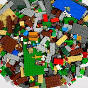 Può includere: Un assortimento colorato di mattoncini di plastica di varie forme e dimensioni. I mattoncini sono principalmente verdi, grigi, marroni e rossi, con diverse miniature e accessori. Include una base verde, un forziere e un blocco TNT.