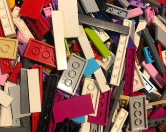 May include: A jumbled assortment of colorful plastic building blocks in various shapes and sizes. The blocks are in shades of red, white, gray, pink, purple, black, green, and yellow. The image shows a variety of rectangular and square blocks.
