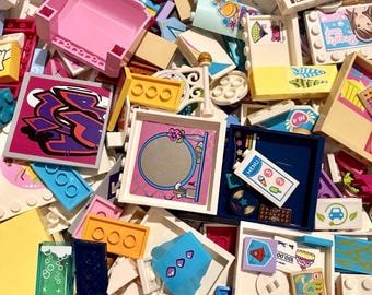 May include: A large collection of assorted plastic building blocks and printed tiles in various colors including pink, blue, yellow, and white. The pieces feature diverse graphics such as a graffiti design, a menu, a mirror, and a beauty shop sign.