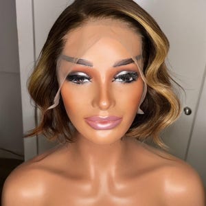 May include: A short, wavy, brown and blonde wig with a lace front. The wig is styled with a side part and has a natural, voluminous look.