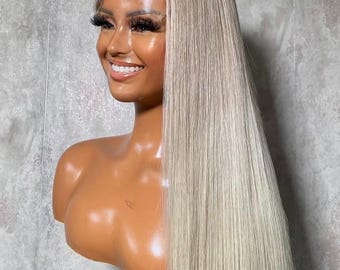 May include: A blonde wig with long, straight hair is displayed on a mannequin head. The wig has a dark root and a light blonde color. The mannequin head is a light brown color.