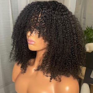 Peut inclure: Une perruque bouclée noire avec une frange. La perruque est coiffée en un bob court et dégradé avec des boucles lâches.