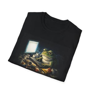May include: Black t-shirt featuring a green frog working on a computer. The frog is sitting at a desk with a keyboard, surrounded by coffee cups and snacks. The computer screen is lit up, and the frog has a focused expression.