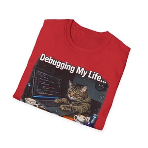 May include: Red t-shirt featuring a tabby cat engrossed in coding on a laptop. The screen shows code, with the text "Debugging My Life..." above. Coffee cups and a can are also visible in the graphic.
