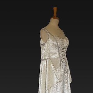 Puede incluir: Un vestido blanco de terciopelo, de hombros descubiertos, con cordones y una larga cola. El vestido tiene un corpi&ntilde;o ajustado y una falda fluida.