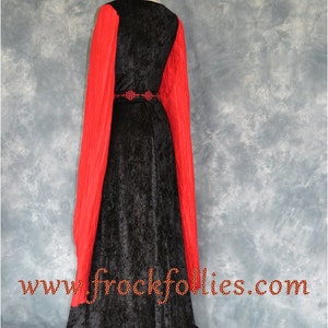 Op de afbeelding: Een zwarte fluwelen jurk met lange rode mouwen en een zwarte riem met een decoratieve gesp. De jurk heeft een sleep en wordt getoond op een mannequin. De tekst "www.frockfollies.com" is zichtbaar onderaan de afbeelding.
