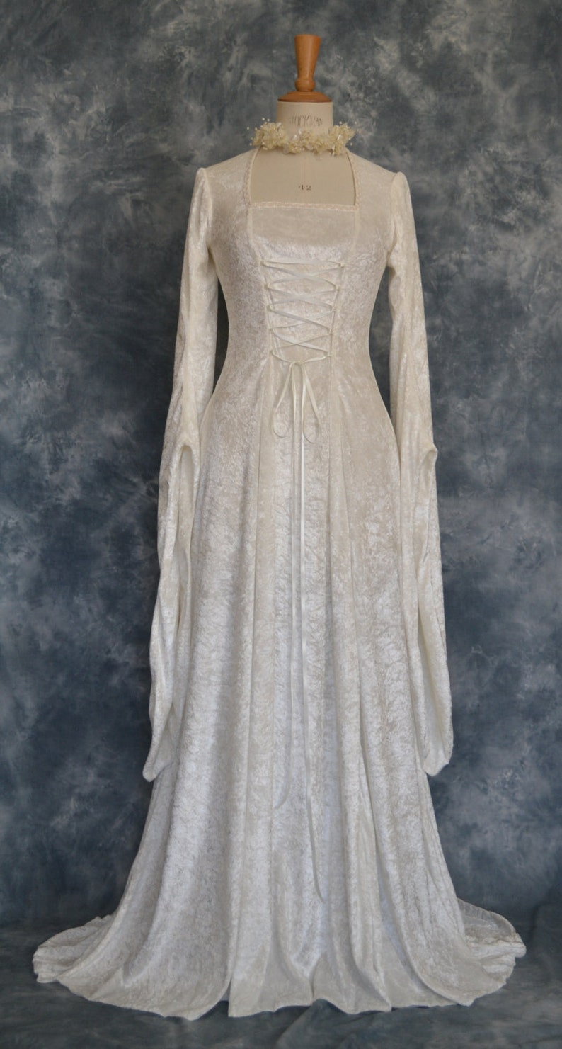 K&ouml;nnte beinhalten: Ein wei&szlig;es Samtkleid mit einem Schn&uuml;rkorsett und langen &Auml;rmeln. Das Kleid hat einen flie&szlig;enden Rock und ein schlichtes Design.