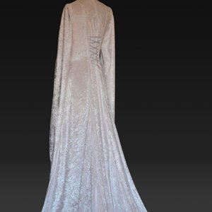 K&ouml;nnte beinhalten: Ein wei&szlig;es Samtkleid mit langen &Auml;rmeln und einem Schn&uuml;rr&uuml;cken. Das Kleid hat einen flie&szlig;enden Rock und ein tailliertes Oberteil.