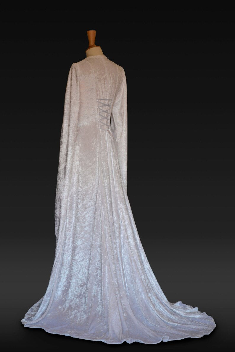K&ouml;nnte beinhalten: Ein wei&szlig;es Samtkleid mit langen &Auml;rmeln und einem Schn&uuml;rr&uuml;cken. Das Kleid hat einen flie&szlig;enden Rock und ein tailliertes Oberteil.