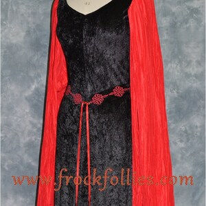 Op de afbeelding: Een zwarte fluwelen jurk met lange rode mouwen en een rode lintgordel. De gordel heeft een decoratief ontwerp van rode knopen. De jurk is op een mannequin en de tekst "www.frockfollies.com" is zichtbaar onderaan de afbeelding.
