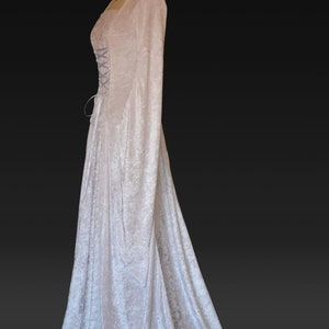 K&ouml;nnte beinhalten: Ein wei&szlig;es Samtkleid mit langen &Auml;rmeln und einem Schn&uuml;rkorsett. Das Kleid hat einen flie&szlig;enden Rock und einen Schlepp.
