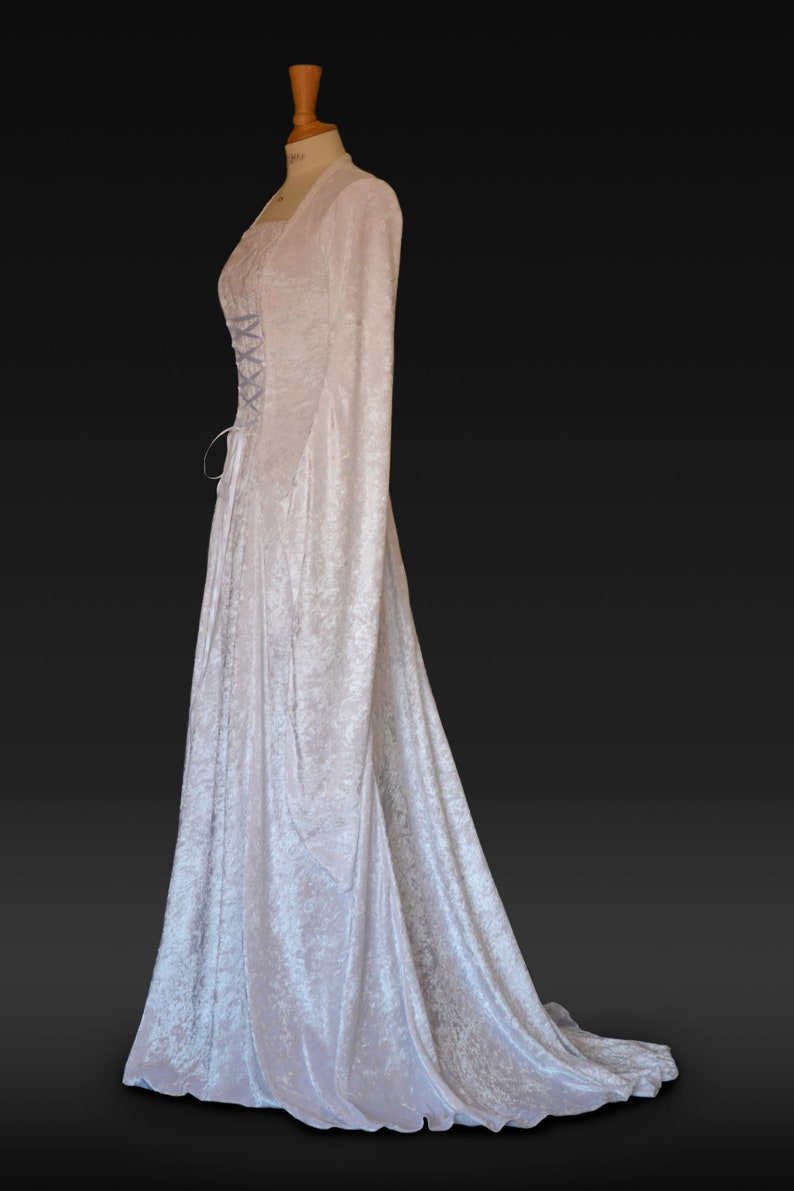 K&ouml;nnte beinhalten: Ein wei&szlig;es Samtkleid mit langen &Auml;rmeln und einem Schn&uuml;rkorsett. Das Kleid hat einen flie&szlig;enden Rock und einen Schlepp.