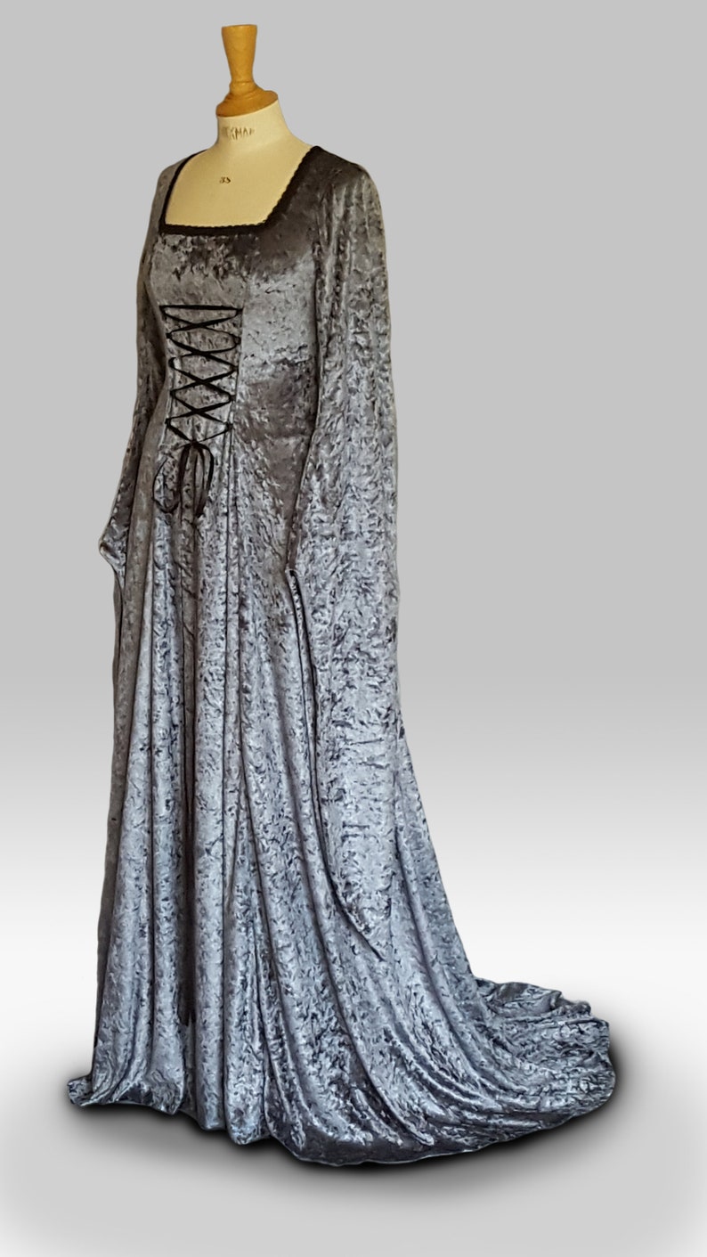 K&ouml;nnte beinhalten: Ein langes, silbergraues Samtkleid mit quadratischem Ausschnitt und einem Schn&uuml;rkorsett. Das Kleid hat lange &Auml;rmel und einen Schlepp.