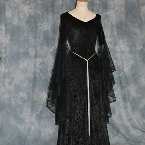 May include: A black velvet gown with long sleeves and a flowing skirt. The gown has a silver beaded belt and a lace overlay on the sleeves.