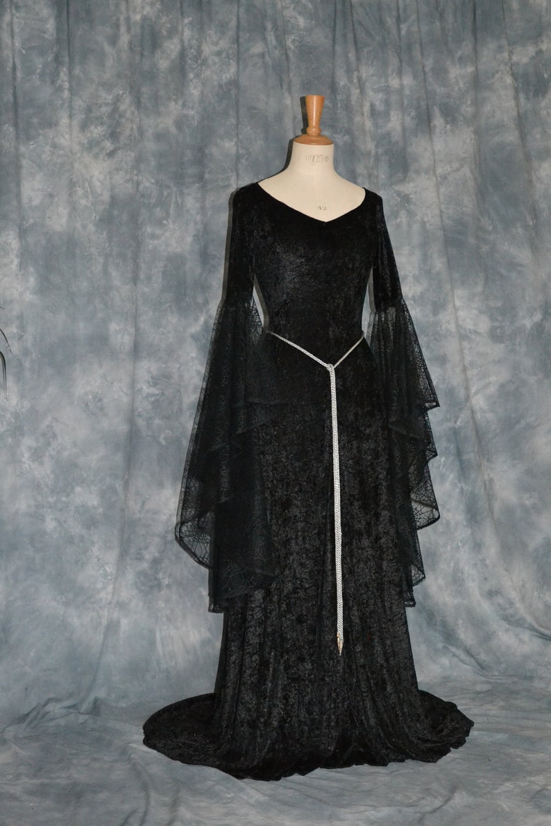 May include: A black velvet gown with long sleeves and a flowing skirt. The gown has a silver beaded belt and a lace overlay on the sleeves.