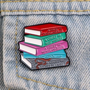 Pode incluir: Um broche de esmalte metálico em forma de uma pilha de cinco livros. O livro vermelho intitula-se A Court of Thorns and Roses, o verde A Court of Mist and Fury, o rosa A Court of Wings and Ruin, o azul A Court of Starlight e o cinzento A Court of Silver Flames.
