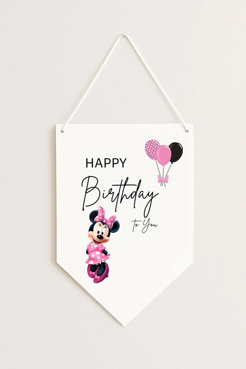 May include: White pennant-shaped wall hanging with a Minnie Mouse illustration and the text "Happy Birthday To You." Minnie Mouse is wearing a pink polka-dot dress and bow. Pink and black balloons are also featured.