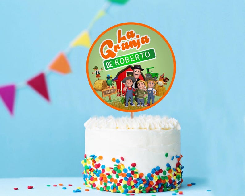 May include: A white cake with colourful sprinkles at the base, topped with a round cake topper. The topper features cartoon characters and the text "La Granja DE ROBERTO" in orange and green.