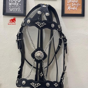 May include: Black leather horse bridle with silver-colored accents, including decorative studs and chain details. The bridle features white stitching and is designed for equestrian use. The image also shows the Horse Tack's logo.