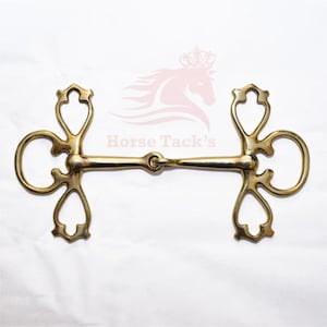 May include: A gold-colored horse bit with decorative heart-shaped cutouts and a curved design. The bit has a central joint and rings on each side. The text "Horse Tack's" is visible in the background.
