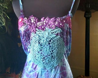 May include: A tie-dye tank top with a crocheted lace overlay and purple and blue accents. The top is displayed on a mannequin.