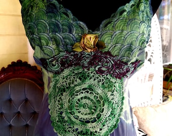 May include: A green and purple tie-dye dress with lace and crochet details. The dress has a green and blue lace bodice with a gold and brown flower accent. The dress also features a green crochet circle in the center.