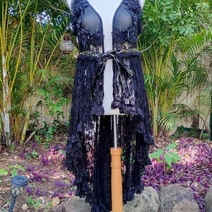 May include: Black lace high-low vest with a plunging neckline, embellished with floral lace appliques and a black satin ribbon tie.