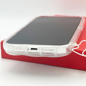 Op de afbeelding: Een transparante telefoonhoes met een verhoogde bumper rond de randen. De hoes is ontworpen om de telefoon te beschermen tegen krassen en vallen. De hoes wordt getoond op een rood oppervlak.