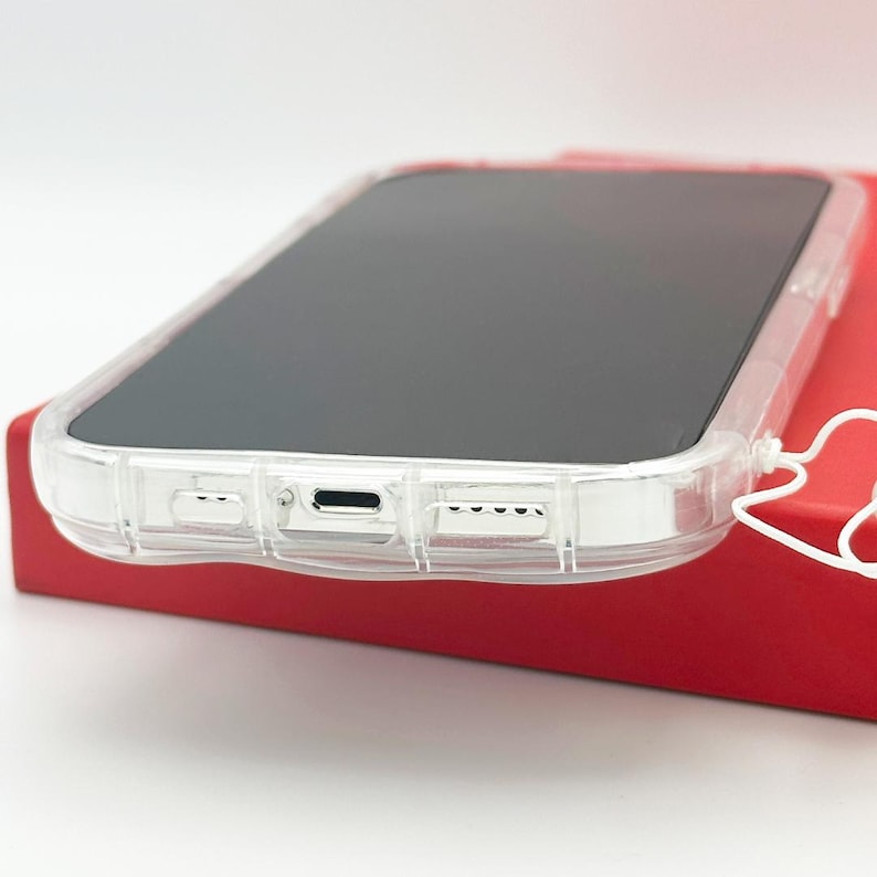 Op de afbeelding: Een transparante telefoonhoes met een verhoogde bumper rond de randen. De hoes is ontworpen om de telefoon te beschermen tegen krassen en vallen. De hoes wordt getoond op een rood oppervlak.