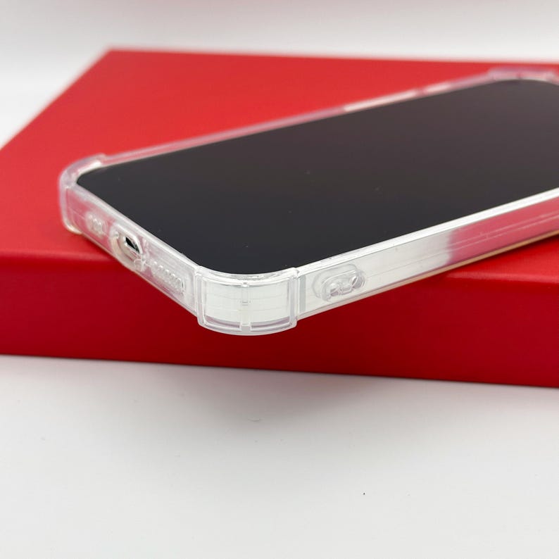 May include: A clear, protective phone case with a black screen, resting on a red surface. The case has a transparent design, showcasing the phone's features. The case has a sleek, modern look.