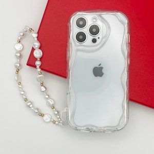 Op de afbeelding: Een transparante telefoonhoes met een golvend ontwerp en een wit Apple-logo. Een witte parel- en gouden ketting is bevestigd aan de hoes.