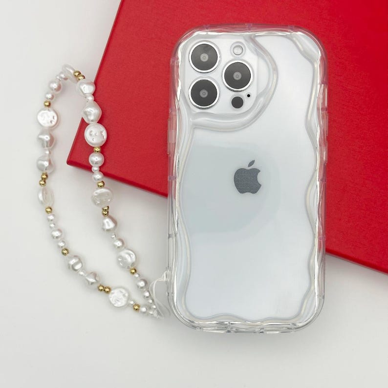 Op de afbeelding: Een transparante telefoonhoes met een golvend ontwerp en een wit Apple-logo. Een witte parel- en gouden ketting is bevestigd aan de hoes.