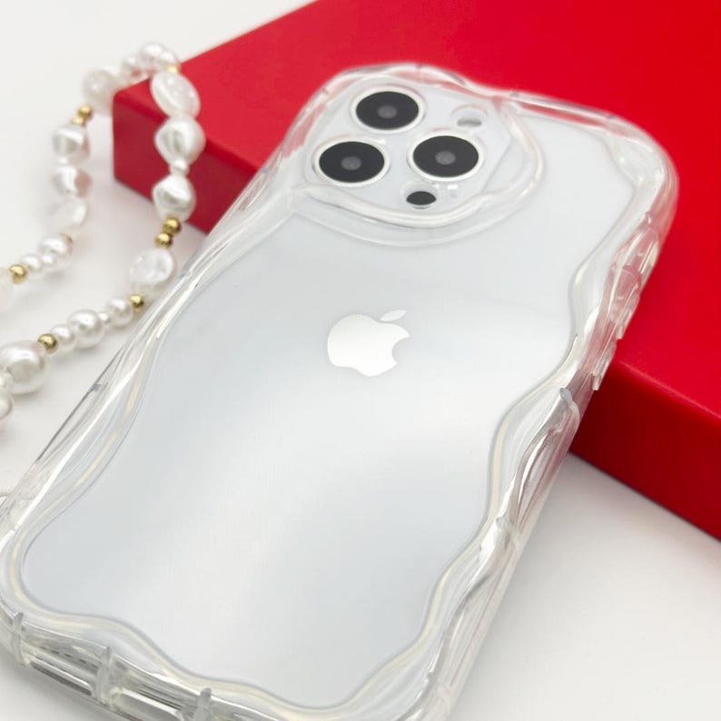 Op de afbeelding: Een transparante telefoonhoes met een golvend ontwerp en een verhoogde camerabult. De hoes is ontworpen voor een iPhone met een transparante achterkant en een wit Apple-logo.