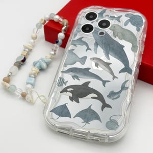 May include: A clear phone case featuring a colourful design of various sea creatures, including dolphins, whales, stingrays, and a sea turtle. The case has a raised lip around the camera lens and a textured grip.