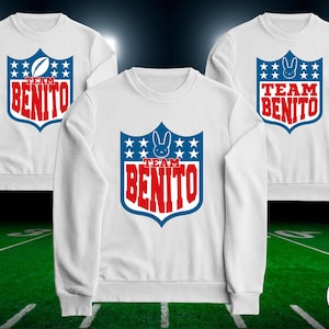May include: White sweatshirts with a graphic design featuring the text "TEAM BENITO" in red, outlined in blue, and a football or bunny icon. The design is set against a blue star-studded background.