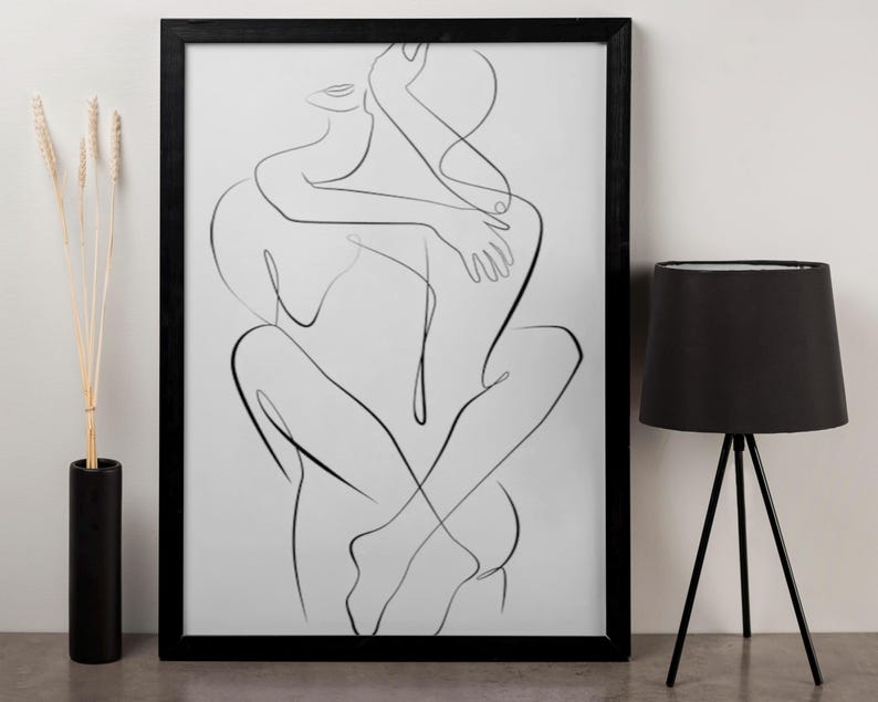 Pu&ograve; includere: Una stampa con cornice nera con un disegno a tratto minimalista di due figure che si abbracciano. L'opera d'arte &egrave; in nero su sfondo bianco. Sono visibili anche una lampada da tavolo nera con base a treppiede e un vaso nero con steli secchi.