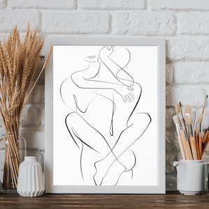 Pu&ograve; includere: Una stampa artistica in bianco e nero incorniciata raffigurante due figure che si abbracciano. L'opera d'arte &egrave; esposta su una superficie di legno con vasi e spighe di grano. Lo sfondo &egrave; un muro di mattoni bianchi.