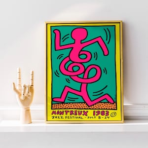 May include: Framed art print with a pink figure on a teal background, outlined in black and yellow. The print is labelled "MONTREUX 1983 JAZZ FESTIVAL - JULY 8-24". A wooden hand sculpture is next to the framed art.