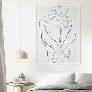 Pu&ograve; includere: Una stampa artistica in bianco e nero incorniciata raffigurante due figure che si abbracciano. L'opera d'arte &egrave; esposta sopra un letto con biancheria da letto bianca e un piumino grigio. Una lampada a sospensione rotonda in legno pende dal soffitto e un piccolo tavolino con piante &egrave; nelle vicinanze.