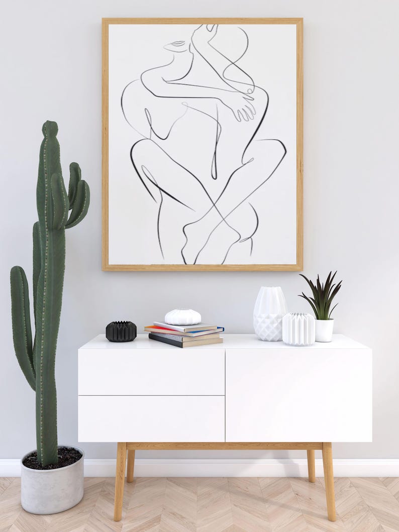 Pu&ograve; includere: Un'opera d'arte in bianco e nero incorniciata, raffigurante due figure che si abbracciano. L'opera &egrave; appesa sopra un mobile bianco con gambe in legno, adornato con vasi decorativi, libri e una piccola pianta in vaso. Un alto cactus a sinistra.