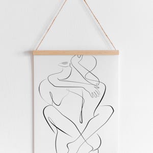 Pu&ograve; includere: Una stampa artistica minimalista a linea nera di due figure che si abbracciano. L'opera d'arte &egrave; esposta su carta bianca, tenuta da barre di legno e sospesa da un cordoncino di spago naturale. Una rappresentazione semplice ed elegante.