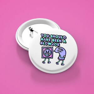 May include: White button badge with a pin back, featuring a cartoon design of a condom and a sperm cell with the text "YOU SHOULD HAVE BEEN A BLOW JOB" in blue and green. The badge is set against a pink background.