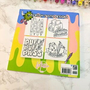 Puede incluir: Un libro para colorear titulado "52 Kush-Tastic Designs" con ilustraciones con temas de cannabis. El libro presenta el texto "Puff Puff Pass" y "Totally Toasted". La portada es verde, rosa y azul con un personaje de dibujos animados.
